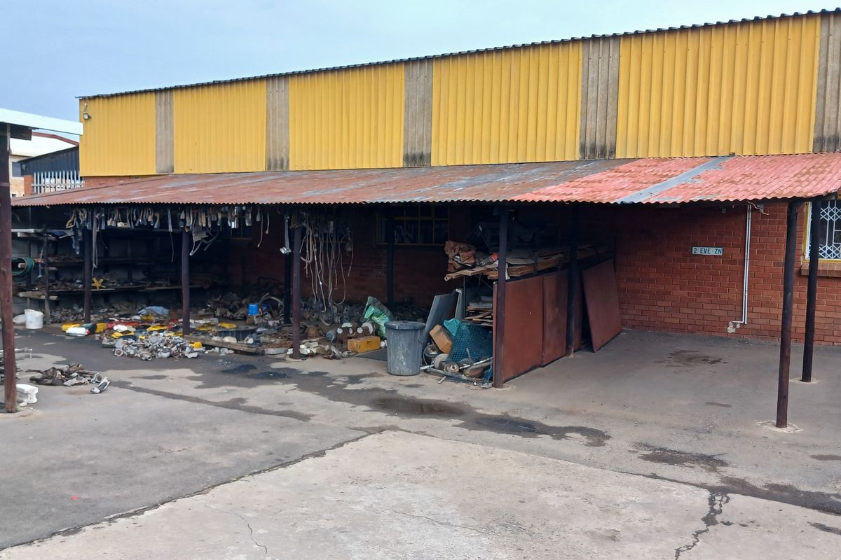 Rear exterior view of a commercial property featuring a covered outdoor storage area with corrugated metal roofing and brick wall construction.