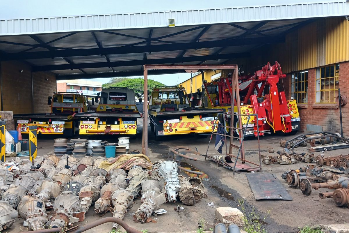 A large industrial garage or workshop space featuring high ceilings, steel structural supports, and brick wall construction, currently utilized for vehicle maintenance and storage.