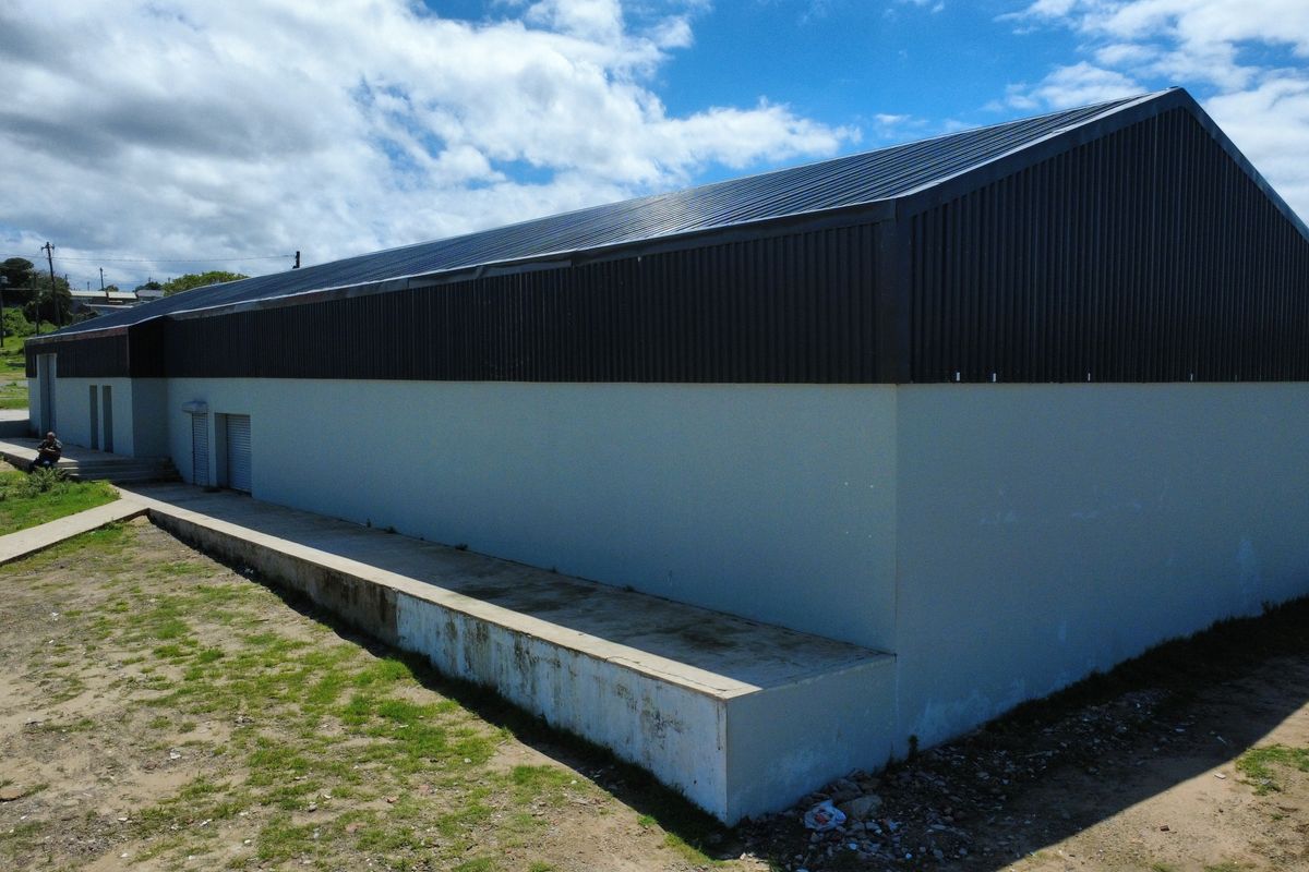 Rear view of a commercial warehouse building featuring a metal roof, concrete loading platform, and roller shutter access doors.