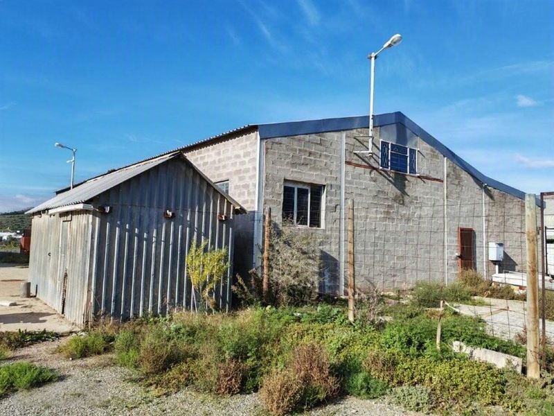 Rear view of a commercial property featuring a cinder block structure and an adjacent corrugated metal storage shed on a gravel lot.