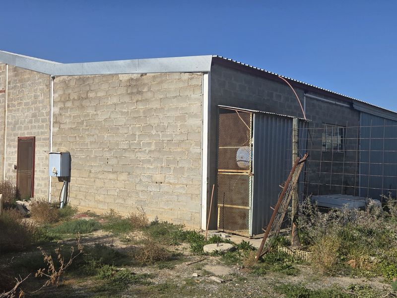 Rear view of a commercial industrial building featuring cinder block construction, corrugated metal roofing, and perimeter wire fencing.