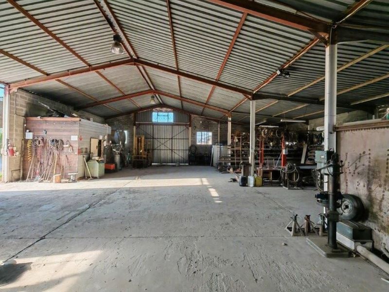 Spacious industrial utility workshop featuring high-clearance corrugated metal roofing, exposed steel trusses, and durable concrete flooring, suitable for storage or manufacturing operations.