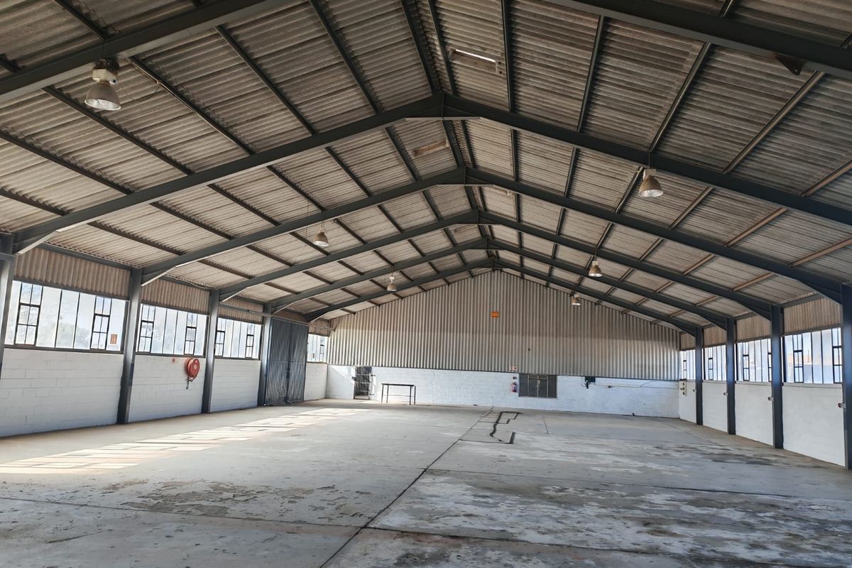 Spacious industrial warehouse featuring a high-clearance steel portal frame, corrugated metal roofing, concrete flooring, and ample natural light through steel-framed windows.