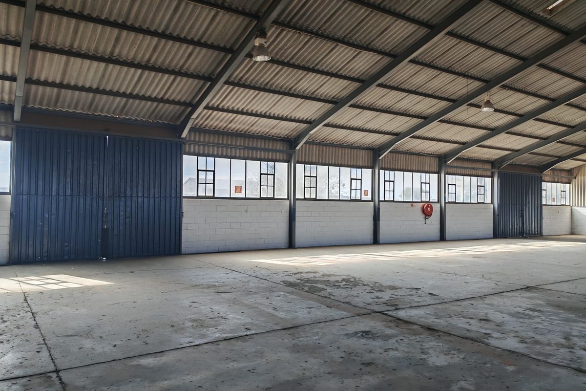Spacious industrial warehouse unit featuring high ceilings, concrete flooring, large sliding access doors, and ample natural light through steel-framed windows.