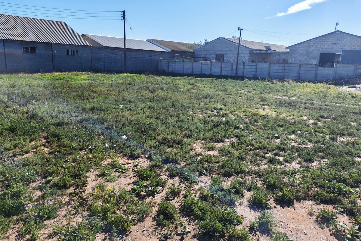 An expansive, undeveloped industrial plot featuring a precast concrete boundary wall and surrounding industrial warehouse structures.