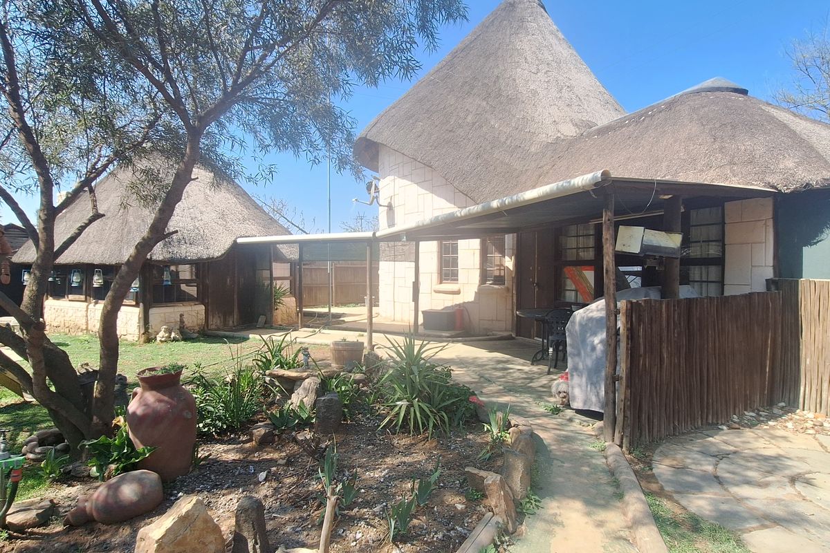 Rear exterior view of a property featuring traditional thatched roof structures, stone walls, and a covered patio area with a paved garden walkway.