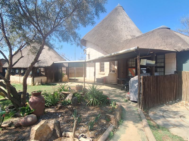 Rear exterior view of a property featuring traditional thatched roof structures, stone walls, and a covered patio area with a paved garden walkway.
