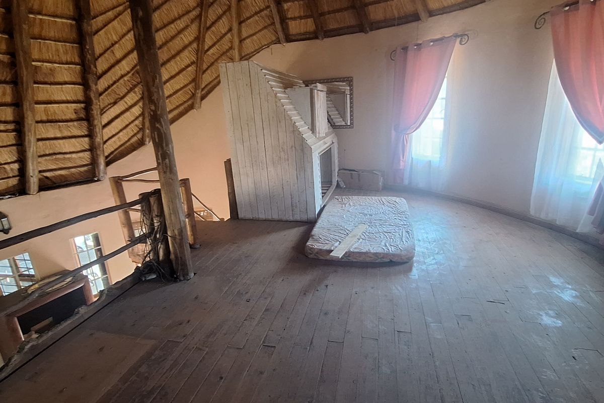 A rustic mezzanine bedroom featuring exposed thatch roofing, timber support beams, and wooden flooring, offering a unique architectural space with potential for renovation.