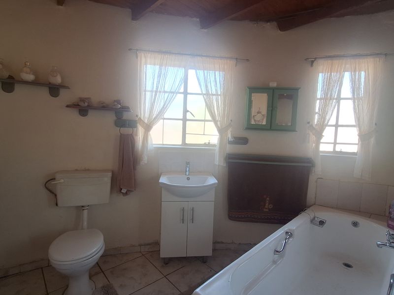 A bathroom featuring exposed timber ceiling beams, a vanity basin, a built-in bathtub, and a toilet, with dated finishes and worn floor tiles.