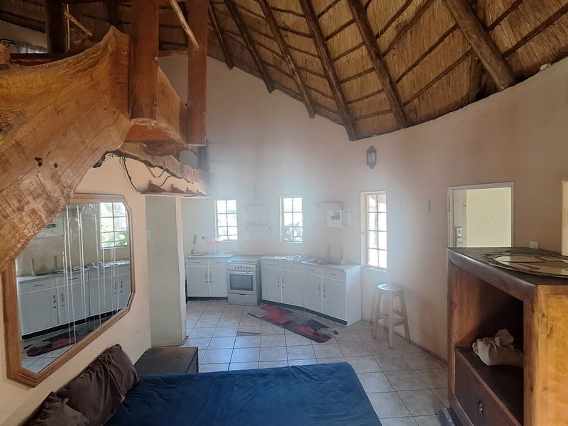 Open-plan living area featuring a traditional thatched roof with exposed timber rafters, tiled flooring, and a functional kitchen space with built-in cabinetry.