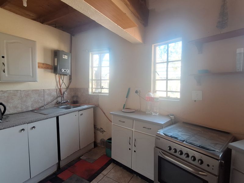 A compact kitchen featuring built-in cabinetry, a stainless steel sink, a freestanding stove, and exposed timber ceiling beams, requiring cosmetic updates to finishes.