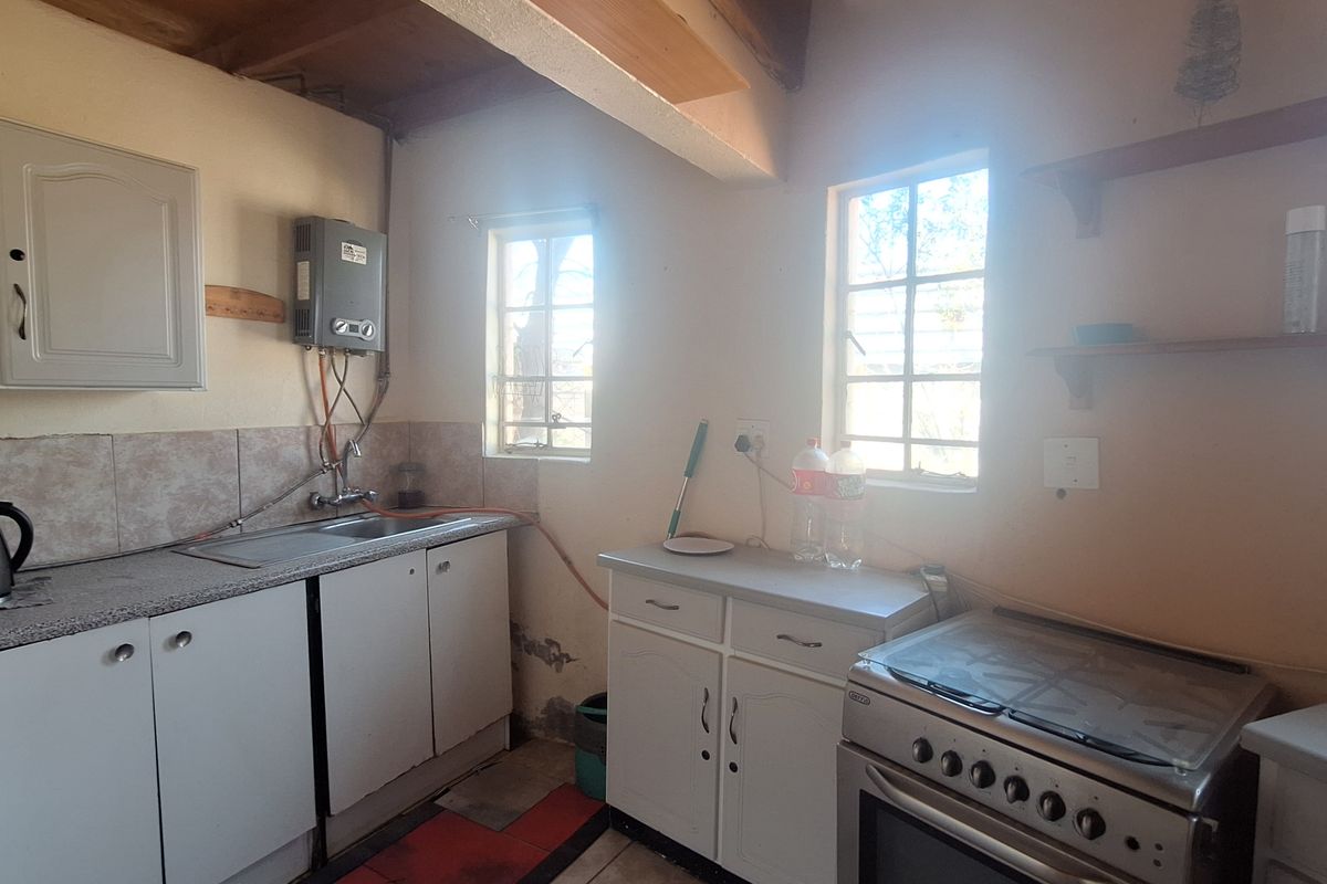 A compact kitchen featuring built-in cabinetry, a stainless steel sink, a freestanding stove, and exposed timber ceiling beams, requiring cosmetic updates to finishes.