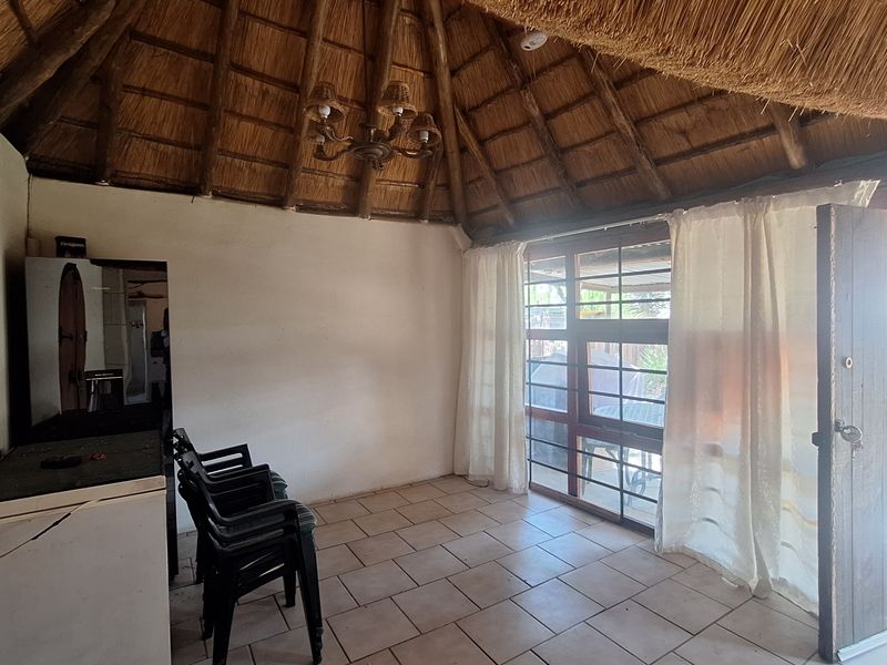 A rustic living area featuring a high vaulted thatched roof with exposed timber rafters, tiled flooring, and direct access to an outdoor space.