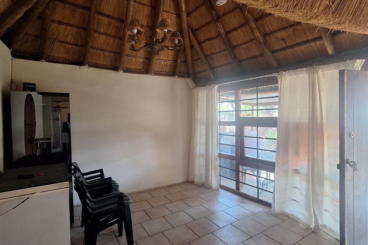 A rustic living area featuring a high vaulted thatched roof with exposed timber rafters, tiled flooring, and direct access to an outdoor space.
