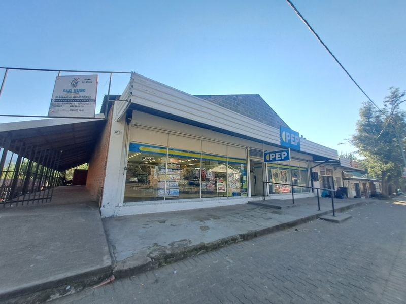 Commercial storefront featuring large glass display windows, prominent signage, and a concrete walkway entrance in a street-facing location.