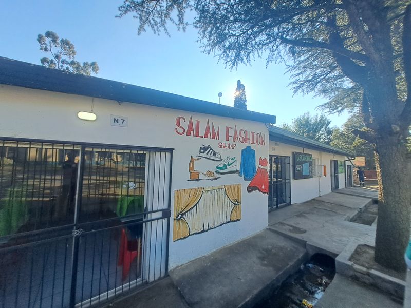 Front exterior view of a commercial retail unit featuring painted signage, security gates, and a concrete walkway.