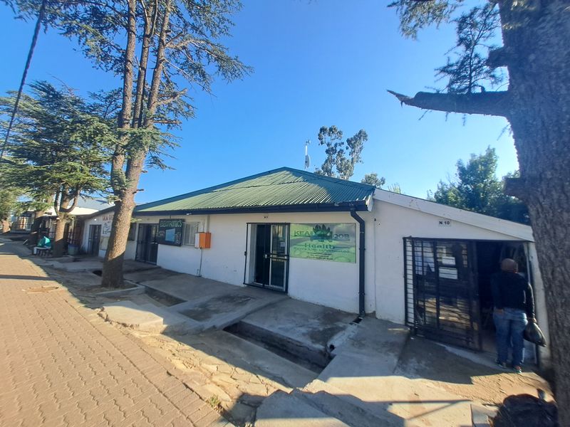 Front exterior view of a commercial building featuring a corrugated metal roof, security gates, and paved walkway access.