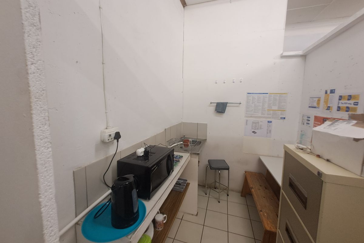 A compact commercial kitchenette featuring a stainless steel sink, tiled splashback, and tiled flooring, suitable for staff use.