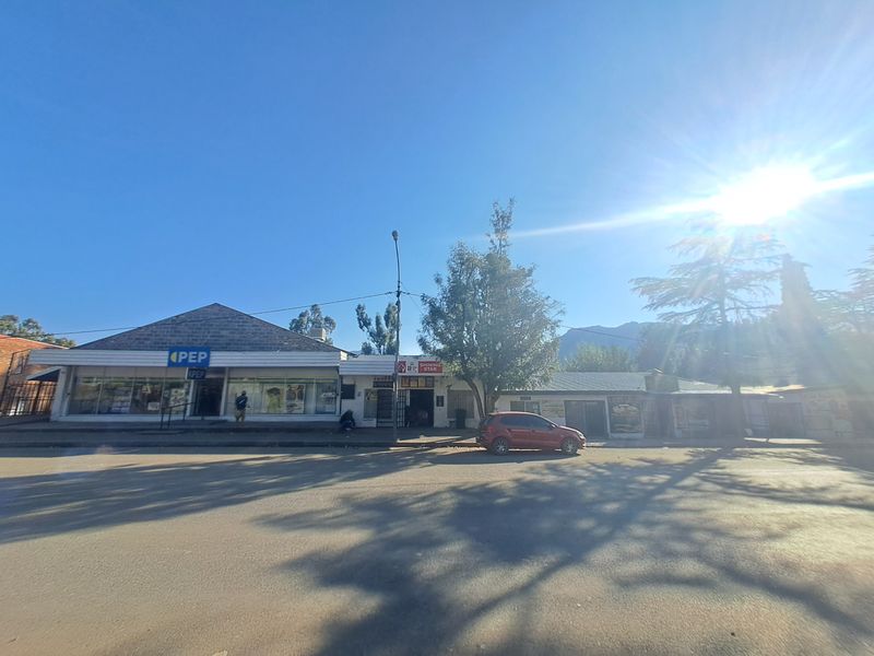 A street-level view of a commercial retail building featuring multiple storefronts with signage and an adjacent paved parking area.