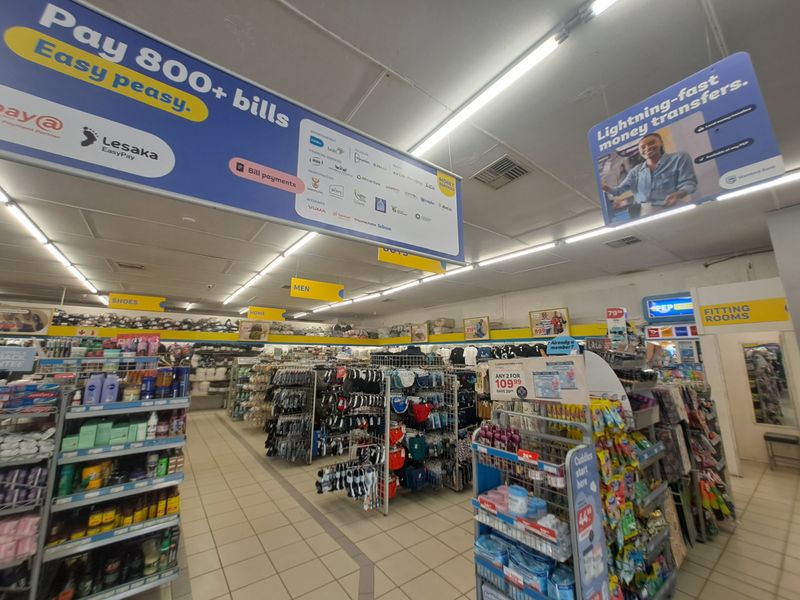 Interior view of a commercial retail store featuring tiled flooring, suspended ceiling with fluorescent lighting, and various retail shelving units.