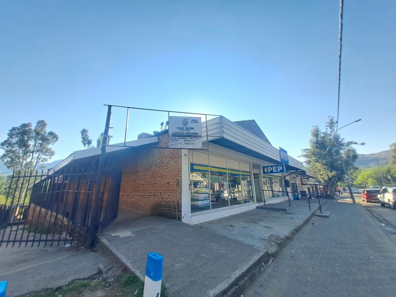 Commercial storefront featuring a brick facade, large display windows, and metal security fencing, situated along a paved street.