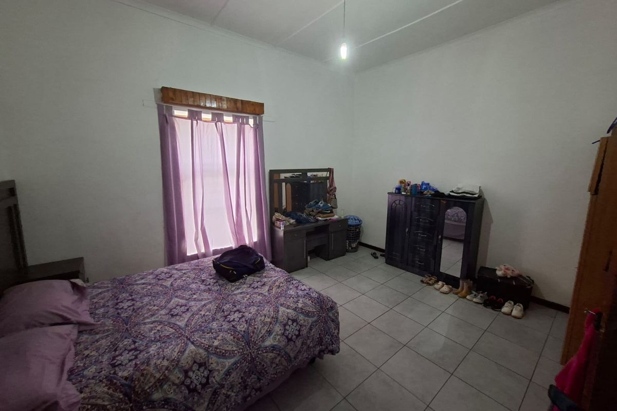A functional bedroom featuring tiled flooring, a single window with wooden trim, and standard ceiling lighting.