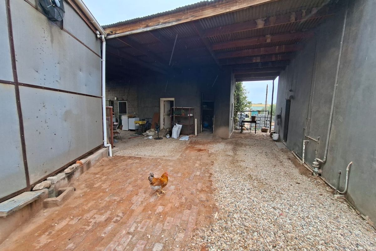 A covered outdoor utility area featuring a mix of brick and gravel flooring, corrugated metal roofing, and exposed structural walls.