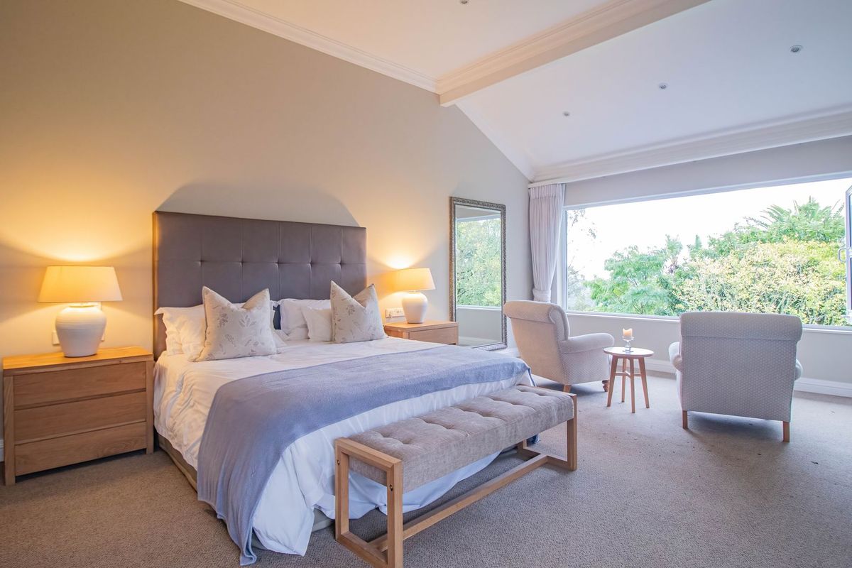 A spacious bedroom featuring high vaulted ceilings, neutral wall finishes, plush carpeting, and a large window offering scenic garden views.