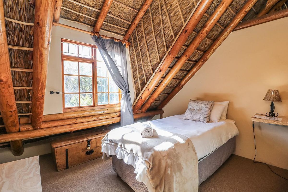 Cozy bedroom featuring a unique thatched roof with exposed timber rafters and a timber-framed window, creating a rustic and inviting atmosphere.