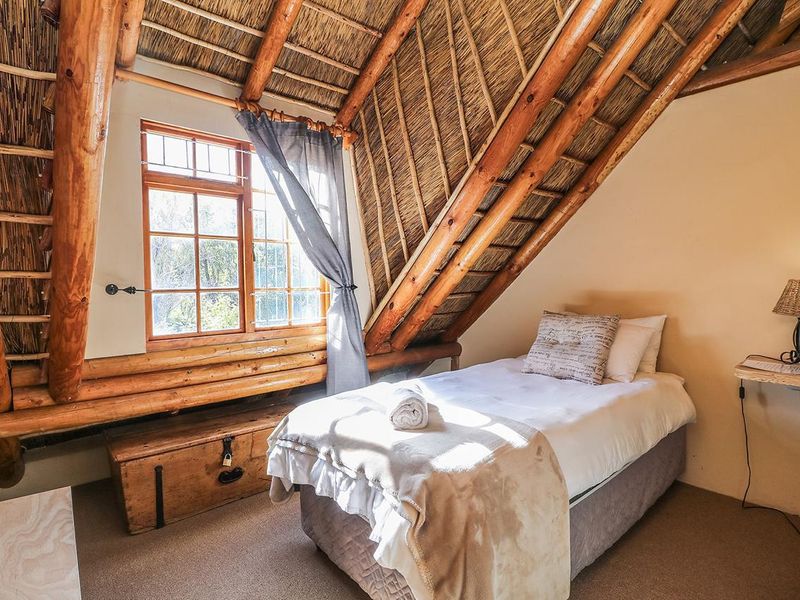 Cozy bedroom featuring a unique thatched roof with exposed timber rafters and a timber-framed window, creating a rustic and inviting atmosphere.