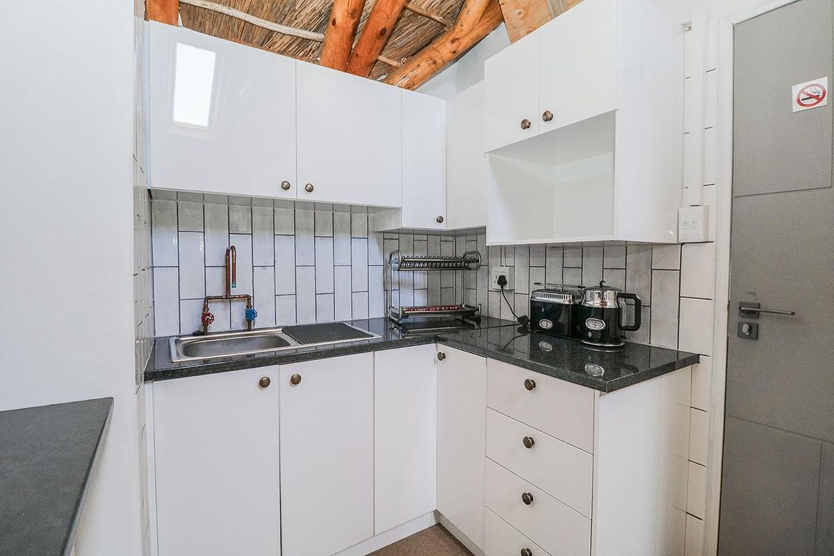 Compact kitchen featuring white cabinetry, granite countertops, subway tile backsplash, and a unique exposed timber and thatched ceiling design.