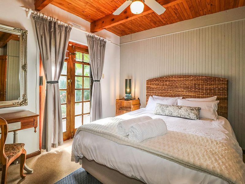 A cozy bedroom featuring a timber ceiling with exposed beams, ceiling fan, and timber-framed french doors providing natural light and garden access.