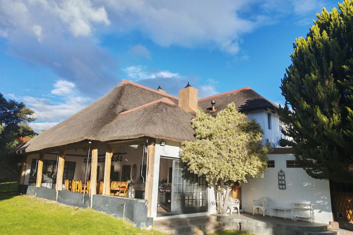 Rear view of a guest house featuring a traditional thatched roof, a spacious covered patio with timber supports, and direct access to the garden.