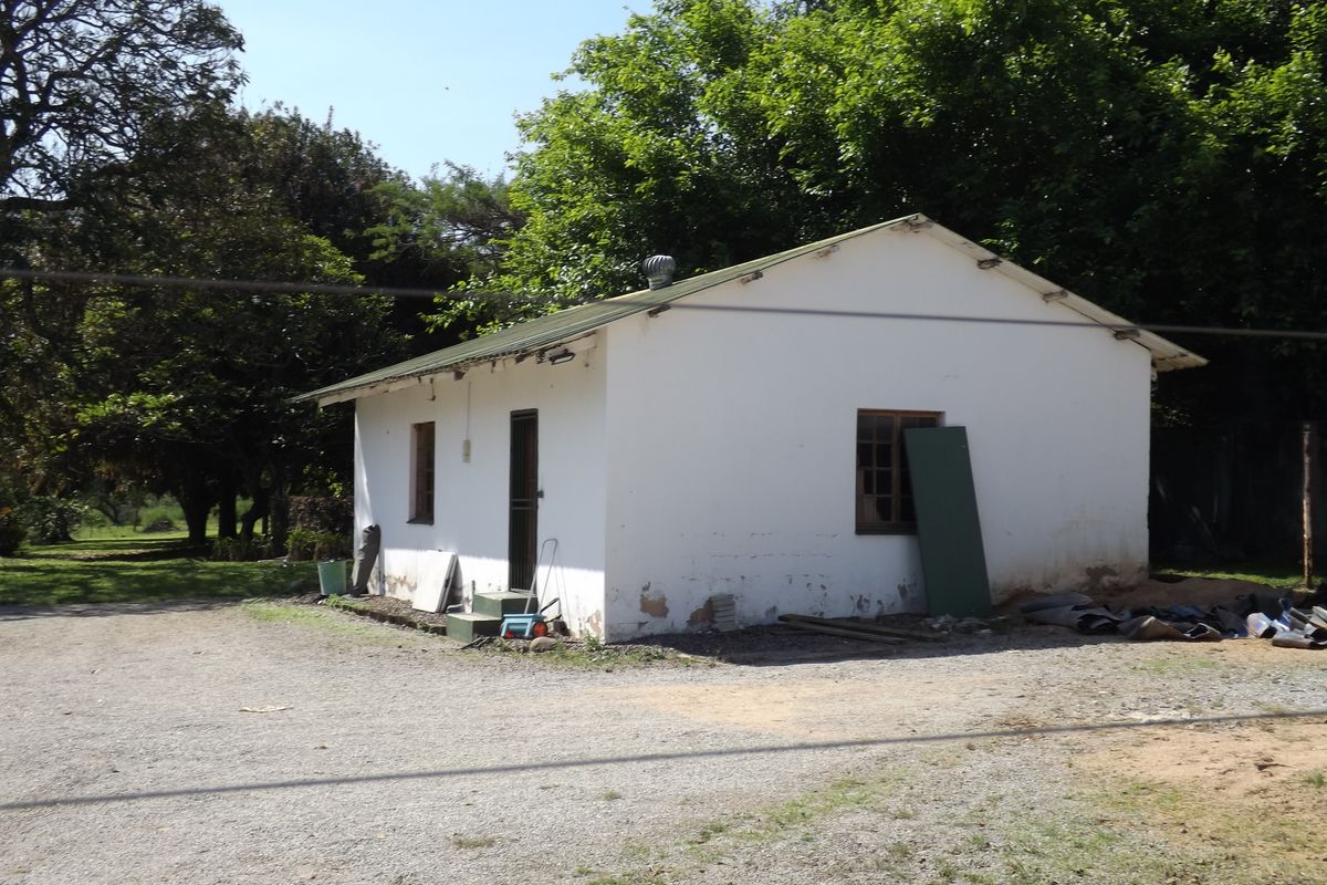 Rear view of a small farm outbuilding featuring a metal roof, security gate, and timber frame windows, set on a gravel yard.
