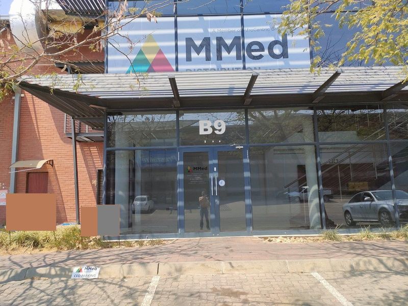Front entrance of an industrial building featuring a modern glass facade, metal awning, and paved parking area.