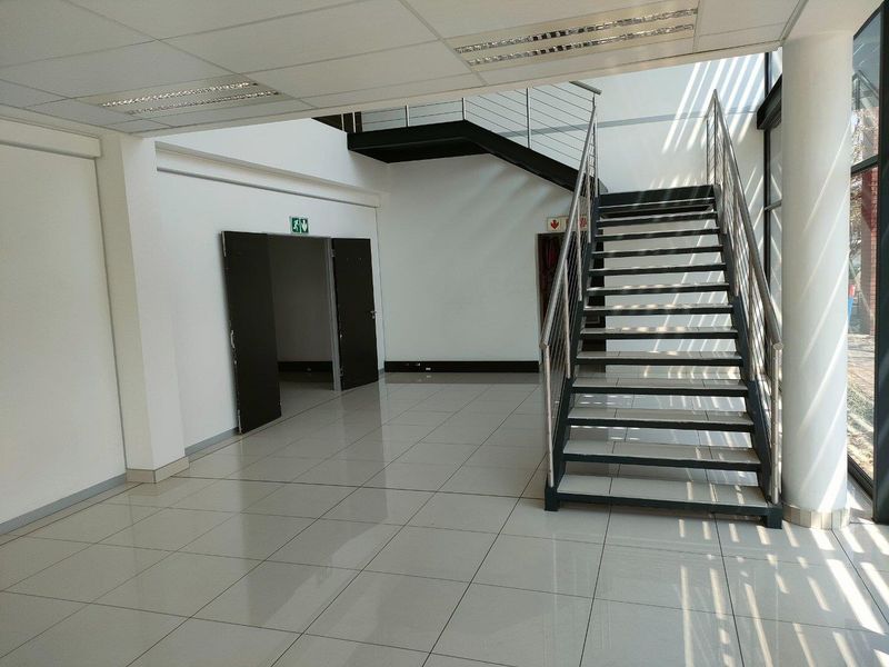 Spacious industrial entrance foyer featuring polished tiled flooring, a modern metal staircase with stainless steel balustrades, and large windows providing natural light.
