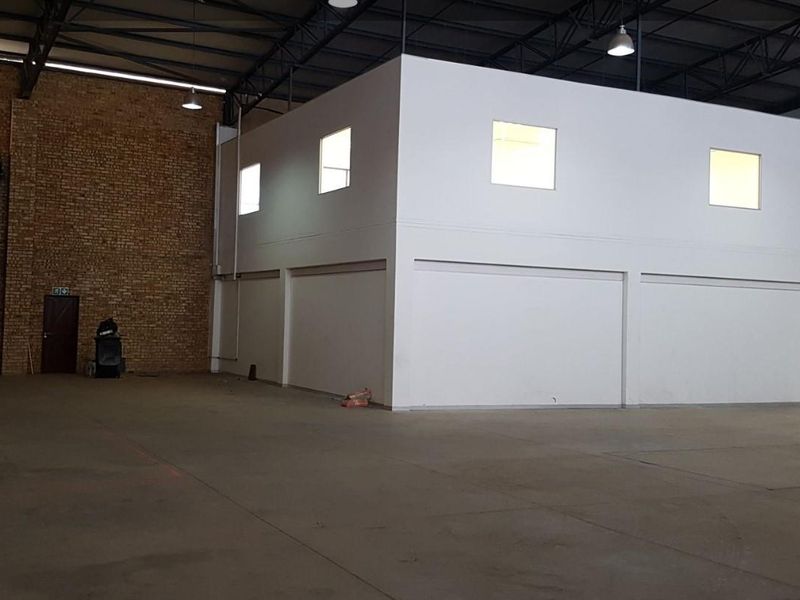 Spacious industrial warehouse unit featuring high ceilings with exposed steel trusses, a mezzanine level, and a large roller shutter door for easy access.