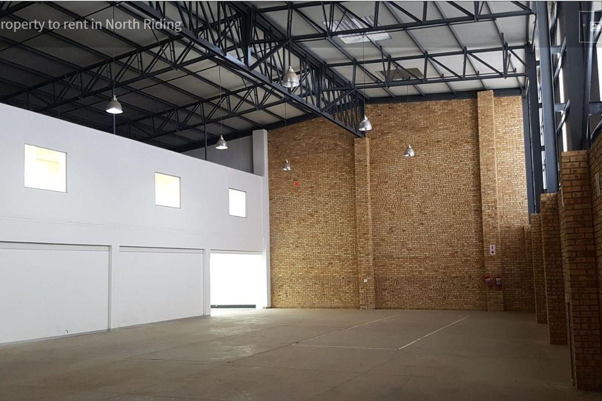 Spacious industrial warehouse unit featuring high ceilings with exposed steel trusses, durable concrete flooring, and a combination of white and facebrick wall finishes.