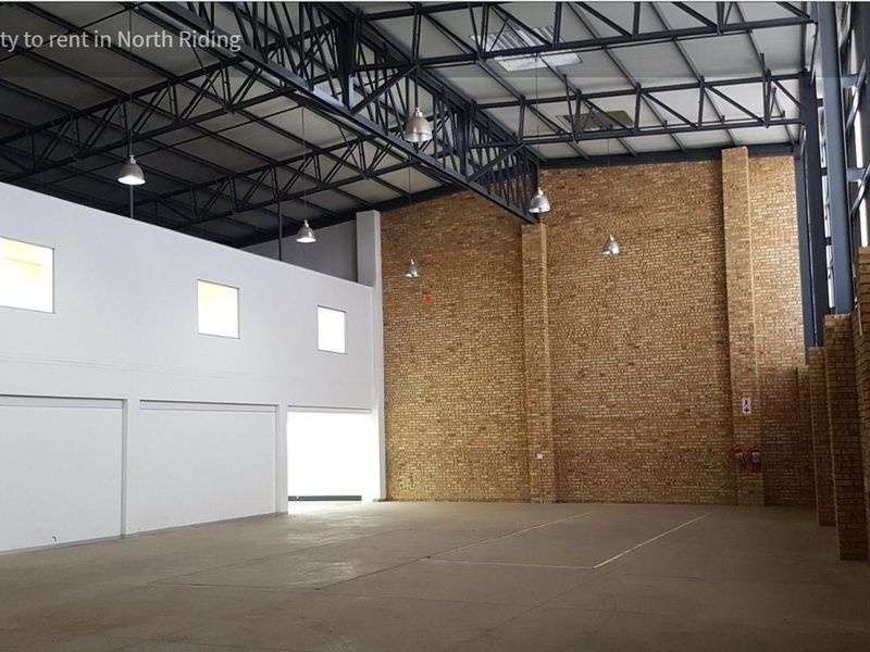 Spacious industrial warehouse unit featuring high ceilings with exposed steel trusses, durable concrete flooring, and a combination of white and facebrick wall finishes.