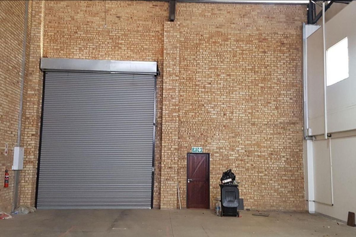 Spacious industrial utility area featuring high ceilings, exposed brick walls, and a large roller shutter door for easy access.
