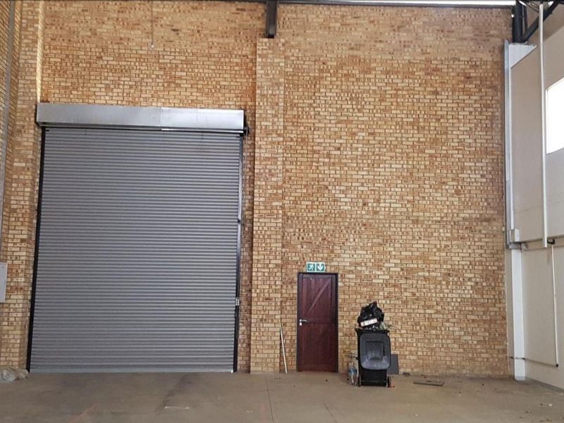 Spacious industrial utility area featuring high ceilings, exposed brick walls, and a large roller shutter door for easy access.