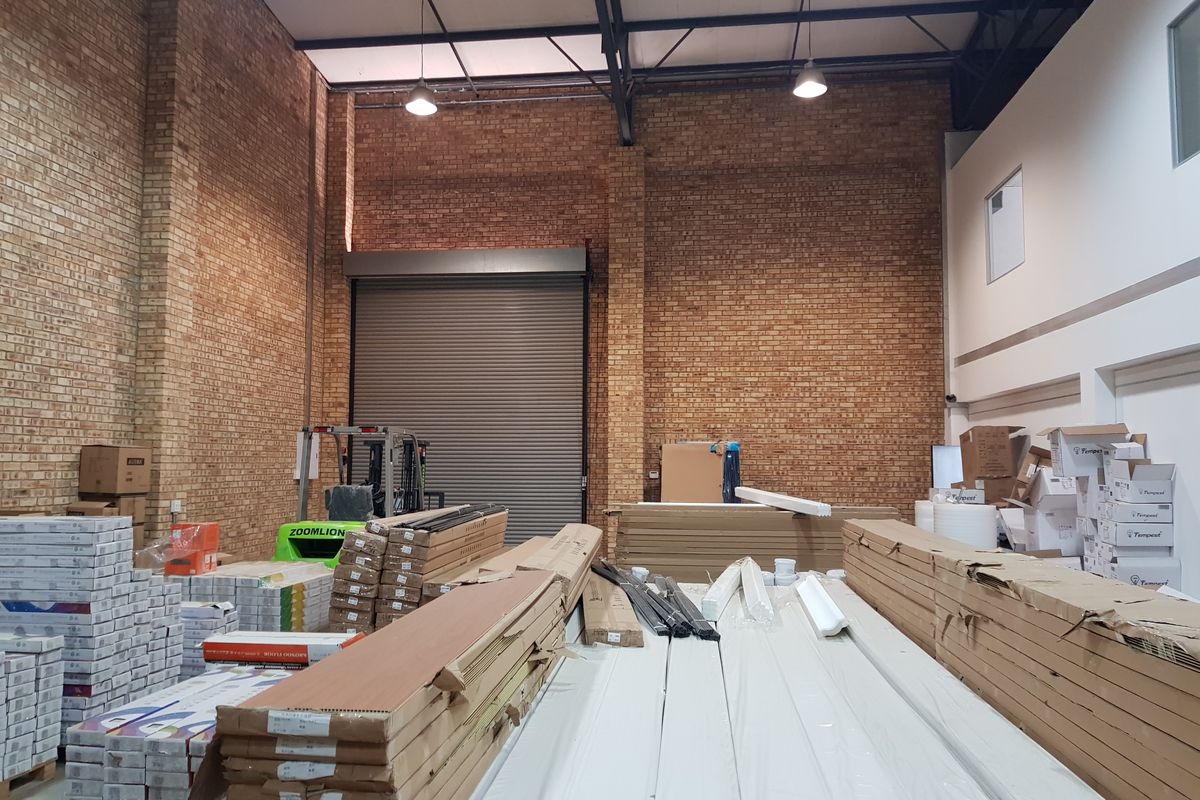 Spacious industrial warehouse unit featuring high ceilings, exposed brickwork, steel roof trusses, and a large roller shutter door for easy access.