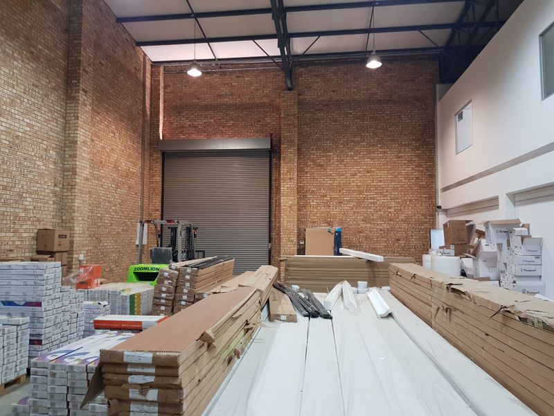 Spacious industrial warehouse unit featuring high ceilings, exposed brickwork, steel roof trusses, and a large roller shutter door for easy access.