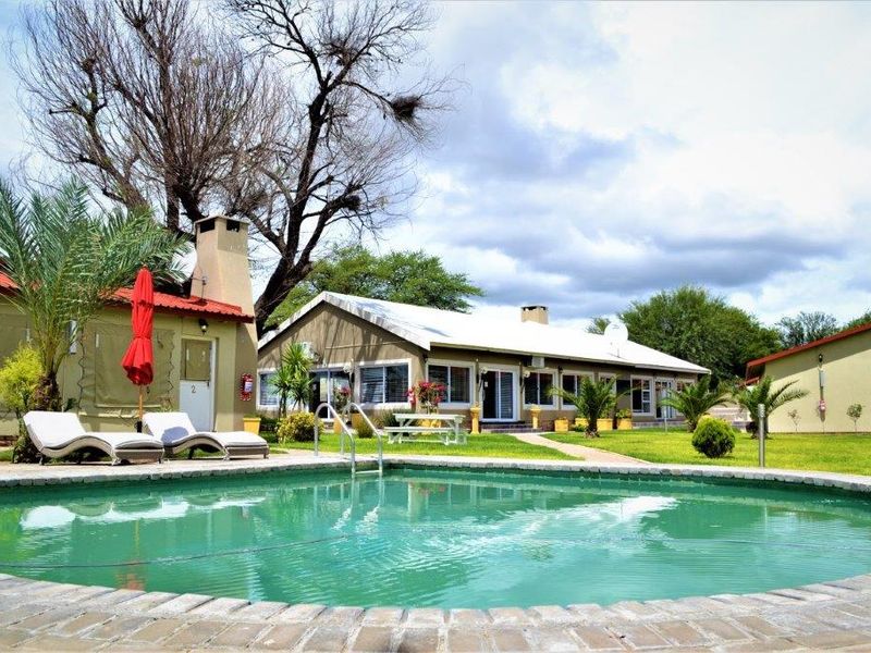 A well-maintained outdoor pool area featuring a circular pool with brick coping, surrounded by a landscaped lawn and guest house buildings.