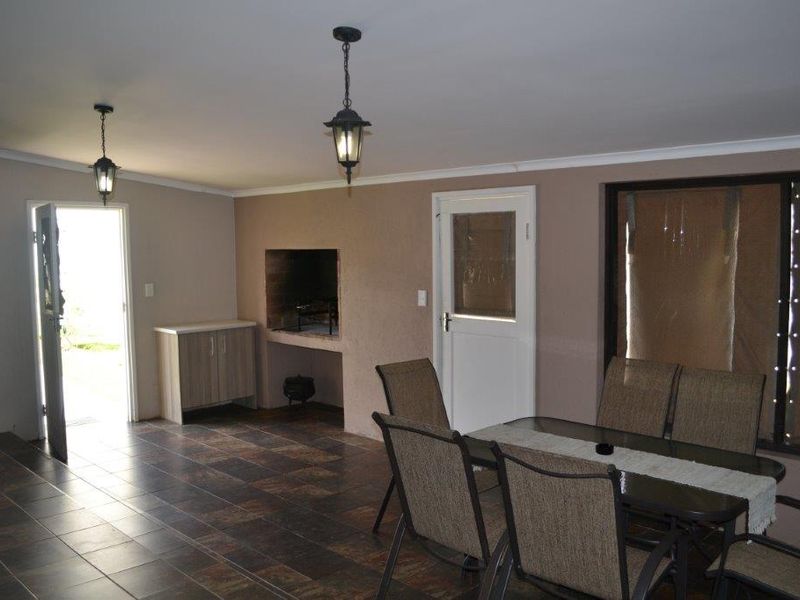 A covered patio area featuring tiled flooring, built-in braai, and direct access to the exterior, providing a functional space for outdoor dining and entertainment.