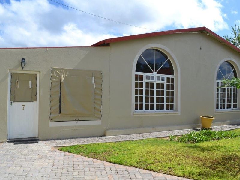 Front exterior view of the guest house featuring arched windows, paved walkway, and protective canvas storm shutters over the entrance and window.