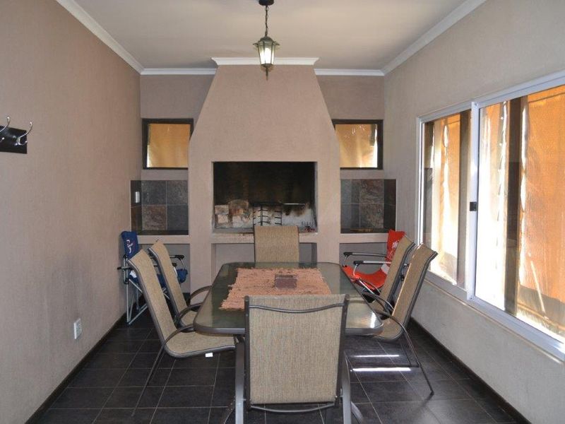 Covered patio area featuring a built-in braai, tiled flooring, and large sliding windows, providing a functional space for outdoor dining and entertainment.
