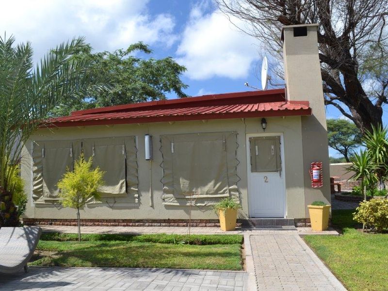 Exterior view of a guest house unit featuring a red corrugated metal roof, brick chimney, and a paved walkway leading to the entrance.