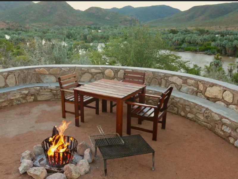 Outdoor patio area featuring a stone retaining wall with integrated bench seating, overlooking a scenic river and mountain landscape.