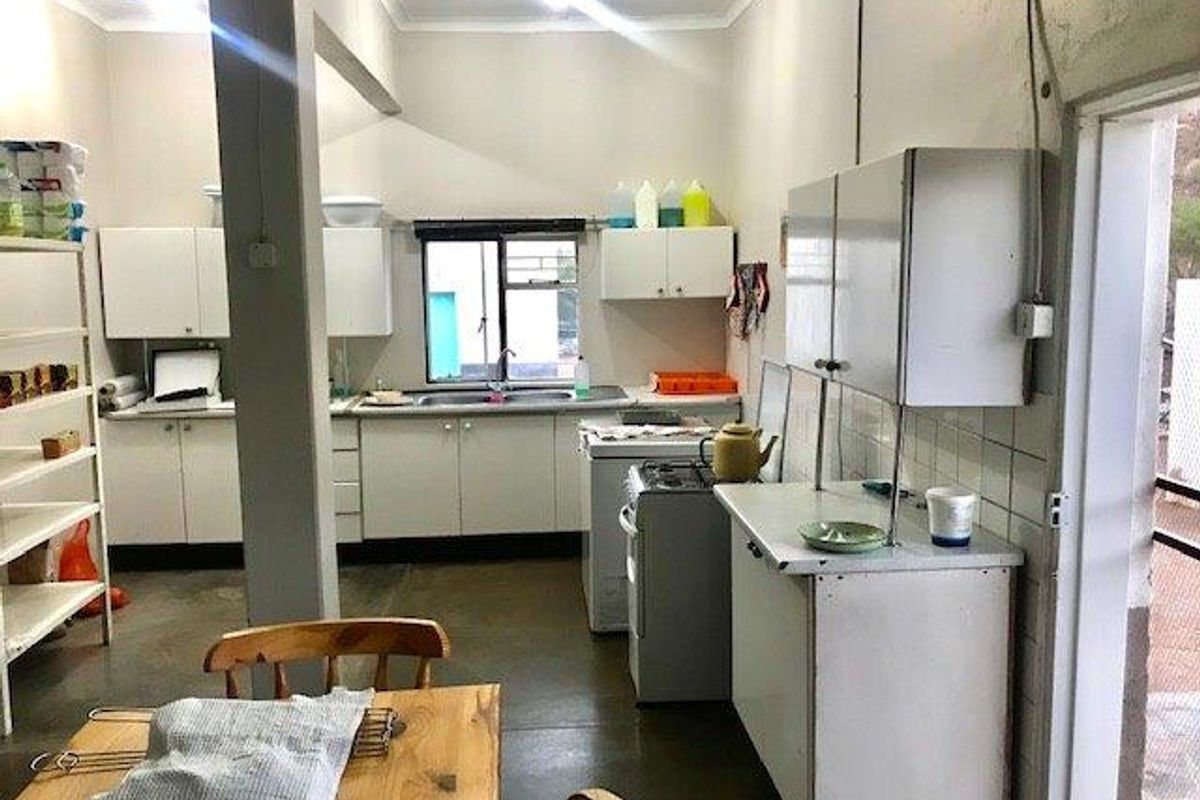 A functional kitchen and scullery area featuring white cabinetry, a stainless steel sink, and a freestanding stove, providing ample storage and workspace.